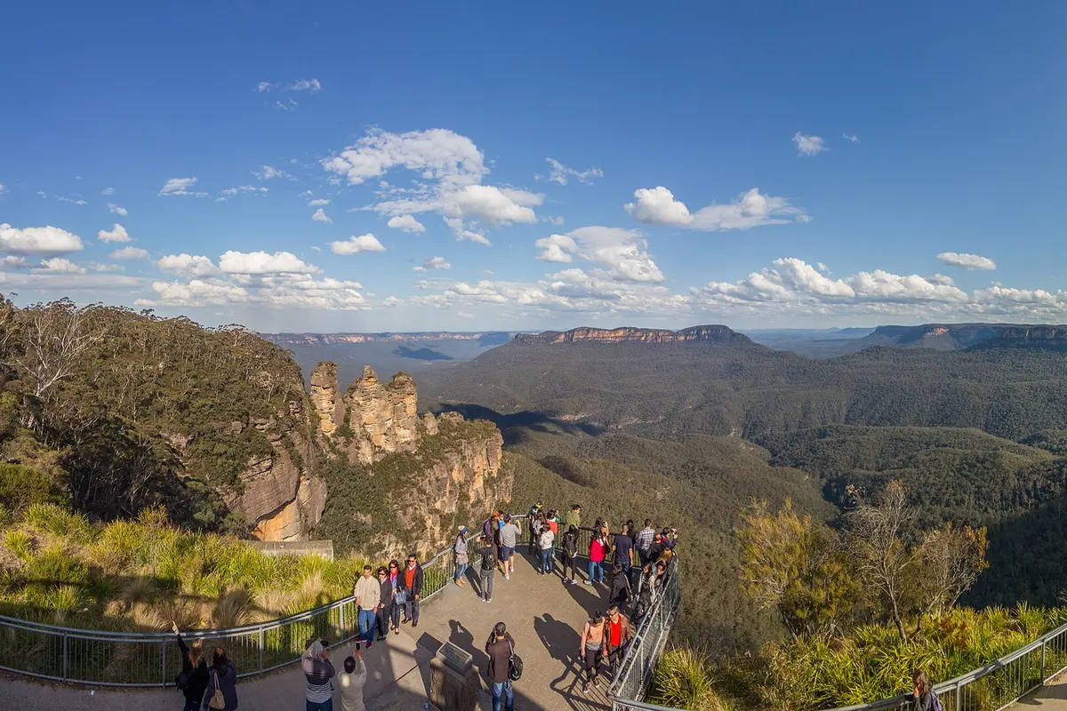 Die Sandsteinzacken der Three Sisters, vom belebten Echo Point Lookout aus über das Jamison Valley hinweg unter blauem Himmel zu sehen
